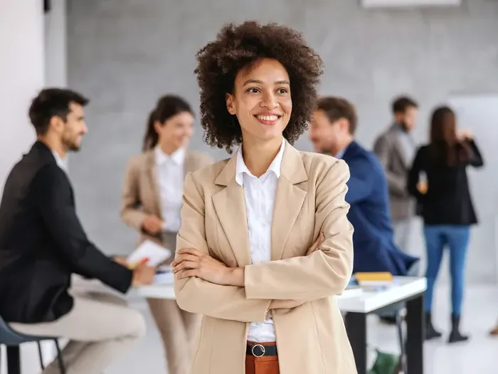 Portrait of a confident young professional standing with folded arms in a modern office during a team meeting